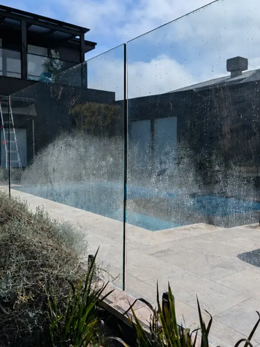 Glass pool fence covered in dried water spots, the pool blurred behind it