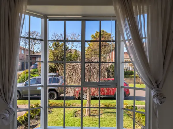 Bay window with sheer curtains tied back, clean glass looking out to a sunny front garden